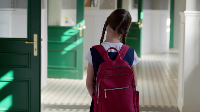 Back view of caucasian schoolgirl with backpack standing in school corridor