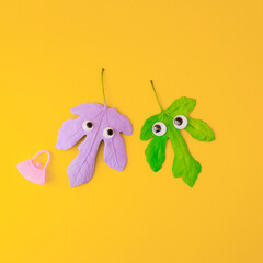 Two autumn leaves in pastel colors that look in love. A funny concept of celebrating a minimal holiday. Yellow autumn background.