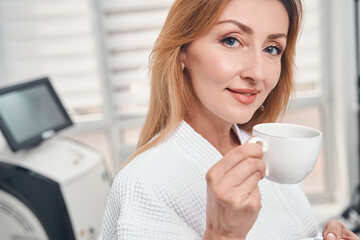 Cheerful woman drinking tea in beautician office