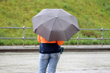 Rain in a city, woman with umbrella standing on a street on road background. Rainy weather, summer or autumn storm