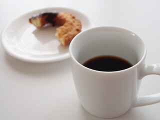 白いカップに入ったコーヒーとちょっと齧られたドーナツ