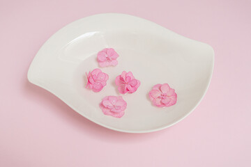 Pink hydrangea petals floating in water with water drops on them on pink paper background. Flat lay, top view. Valentine's background. Floral wallpaper with copy space..