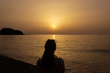 Silhouette of a woman enjoying the sunrise on the beach. Sun rises over the Mediterranean Sea on a lovely summer morning. Selective focus.