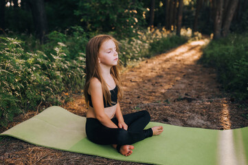 A small, hardworking, beautiful preschool girl, a child athlete sits on a green rug in a lotus...