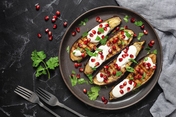 Grilled eggplants with pomegranate, yoghurt garlic sauce and cilantro on a black stone background. Top view, flat lay.