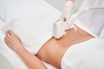 Woman removing hair on abdomen with cosmetologist