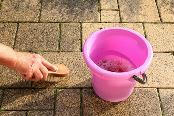 Traditional cleaning of dirty paving stones in the garden with water and a brush.