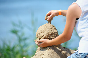 Little girl hands making a sand sculpture on a beach of a river