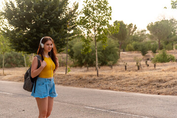 Young caucasian girl listening music in the park with headphones.