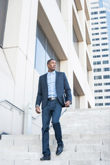 A young handsome black businessman is walking down on steps from a business building..