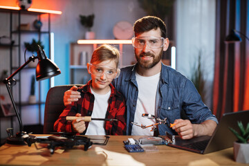 Portrait of happy bearded man with little boy sitting together at table in protective glasses....