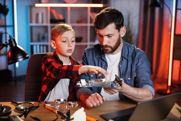 Focused little boy and handsome man repairing display card from modern laptop. Caucasian father helping son to fix portable computer at home.