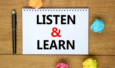 Listen and learn symbol. Words 'Listen and learn' on white note on beautiful wooden table, colored...