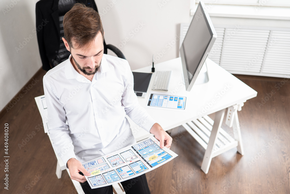 Poster application interface development. man holds a sheet with app layouts. application interface is depi