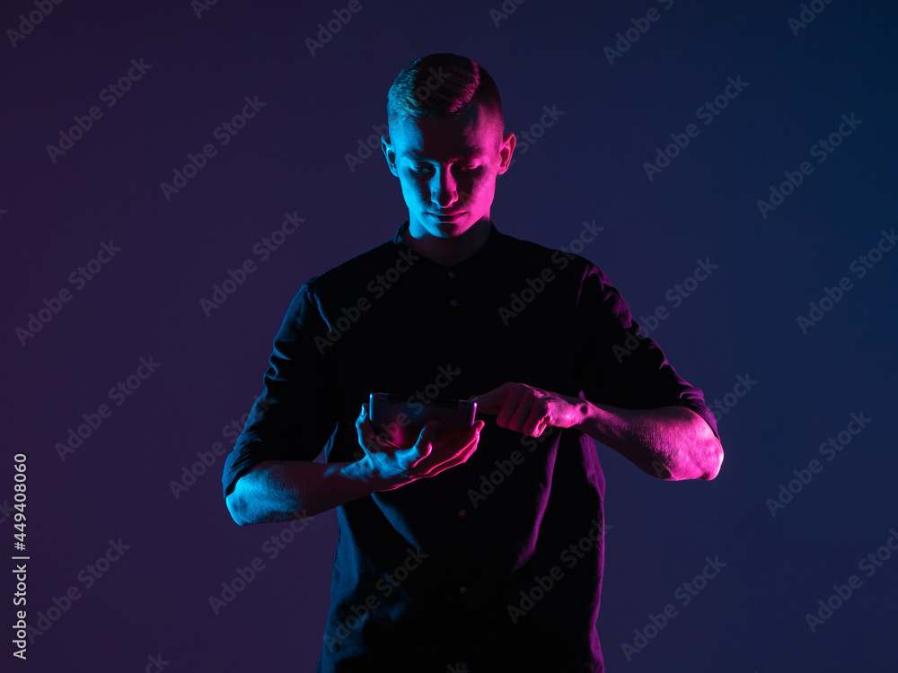 Poster young man uses a tablet computer. guy in dark with a gadget in his hands. man face illuminates light