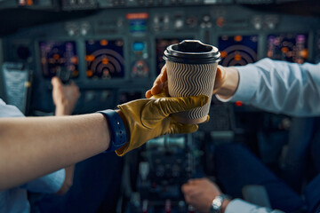 Pilot hand reaching for a disposable paper cup of coffee