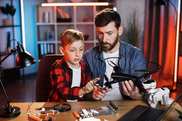 Young caucasian father with his little son fixing modern quadcopter during free time at home....