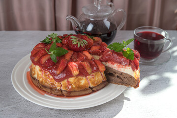 A beautiful cut homemade strawberry dessert with on a plate. Homemade strawberry pie, a cup of tea and a teapot on a bright table.