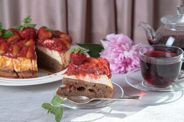 A cut piece of cottage cheese dessert with strawberries on a plate. Homemade strawberry pie, a cup of tea and a teapot on a bright table.