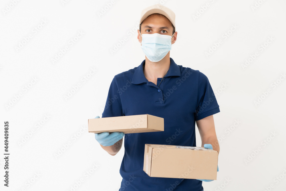 Wall mural Man from delivery service in t-shirt, in protective mask and gloves giving food order and holding boxes over white background.