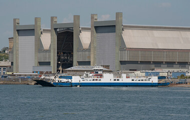 Plymouth, Devon, England, UK. 2021. A roro Torpoint ferry passing the Royal Navy dockyard on the...