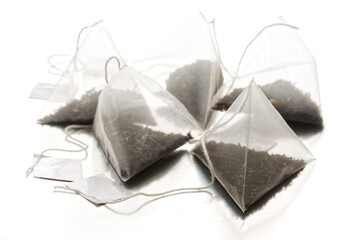 White transparent tea bags-pyramids with black tea, with the addition of fruits and berries, lie on a light reflective background. Shallow depth of field. Selective focusing