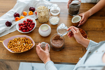 Different ingredients for cooking cereal breakfast on the table. Close up of two women hands cooking together at kitchen.