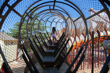 The girl climbs the stairs in the tunnel at a playground.