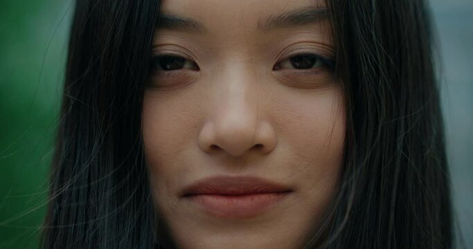 Portrait Face of Girl with Asian Appearance looking into camera. Sensual Ethnic Woman with Long Dark Hair standing outdoors. Expressive Brown Eyes. Beautiful face features of Young Girl. Attractive.