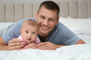 Happy father with his cute baby on bed at home