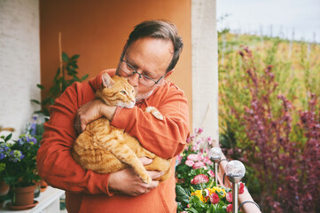 Portrait of middle age man holding cute ginger cat, resting on small cozy balcony