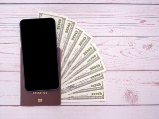 Top view of smartphone and passport book with US dollars banknote on wooden table