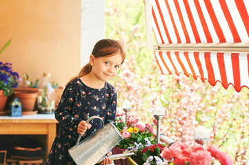 Cute little girl watering plants on small cozy balcony - obrazy, fototapety, plakaty