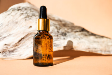 Glass dropper bottle and natural wood on a beige background. Side view, place for text.