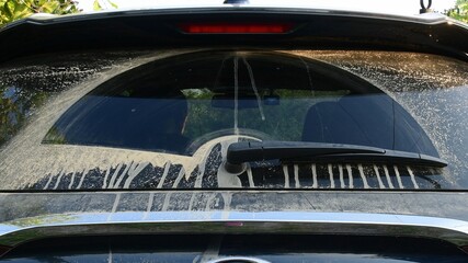 Black car back side and wiper cleaning rear window with sandy drips of dirt due to driving in desert. Dirty car window after off road driving
