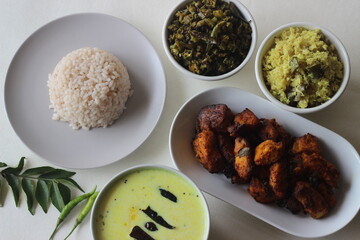 Non vegetarian meals prepared in Kerala style. The serving includes boiled red rice, stir fried onions with coconut, tempered buttermilk, poppadum and air fried basa fish