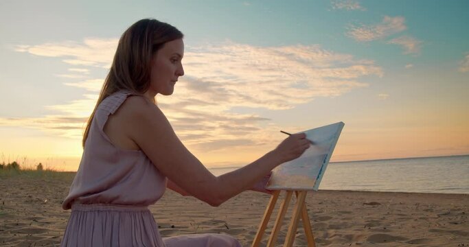 A young woman paints a seascape on canvas with oil paints and a brush. 