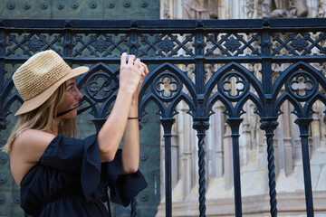 young beautiful woman with hat and map of the city is taking pictures of the cathedral of the city with attention. Travel and holiday concept.