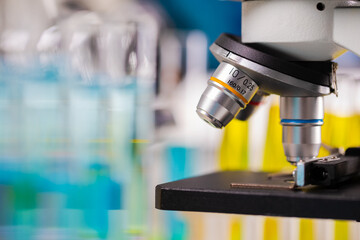 Close up focus of microscope lens with blur colorful background of test tubes and beakers copy space