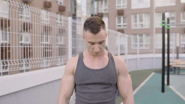 Bodybuilder training on the sports ground and goes restoring breathing after exercise. The athlete goes in for sports on the sports ground on the street.