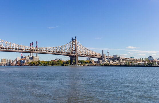 A picture of Ed Koch Queensboro Bridge in New York City, USA. In the picture one can see the East River, the Roosevelt island, Brooklyn and Domino Sugar Refinery and park