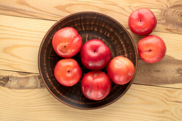Several juicy sweet, red plums in a clay plate on a wooden table, close-up, top view.