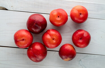 Several juicy sweet, red plums on a wooden table, close-up, top view.