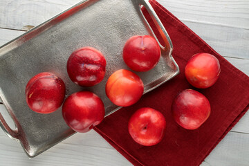 Several juicy sweet, red plums on a metal tray on a wooden table, close-up, top view.
