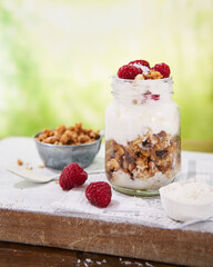 Granola with greek yogurt parfait fresh raspberries, coconut in a glass on wooden table outdoors. Healthy, tasty summer breakfast. Food background with Copy space.