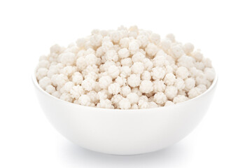 Close-Up of organic small sugar ball candy (nakuldana or elaichidana )  in white ceramic bowl over white background