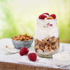 Parfait, granola, greek yogurt,  fresh raspberries, coconut in a glass on wooden table outdoors. Healthy summer breakfast. Food background with Copy space.