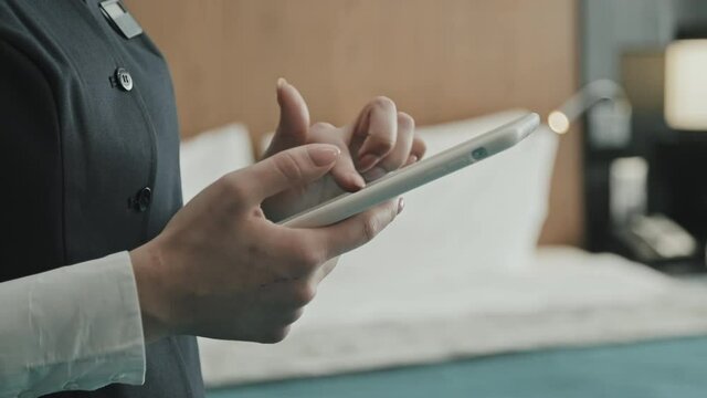 Midsection close-up of unrecognizable female hands of hotel manager using digital tablet standing inside of modern hotel room