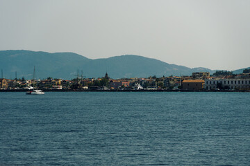 Fototapeta premium Zakynthos, Greece island capital sea view with low rise waterfront buildings. Landscape of houses and stores next to calm sea, with parked tourist buses at the promenade.