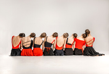 A group of young ballerina girls sitting with their back. They wear black and red ballet clothes. 